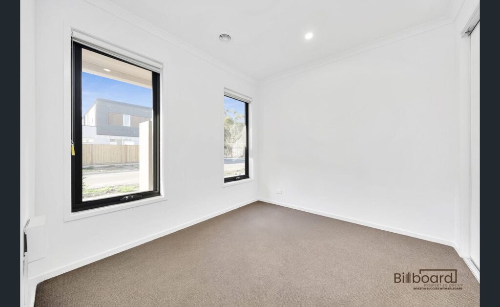 Bright empty bedroom with carpet flooring, white walls and large windows in a contemporary Melbourne home.