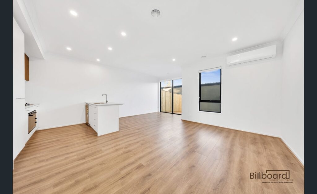 Spacious open living area with timber flooring, split system air conditioning, and modern white kitchen in a contemporary Melbourne home.