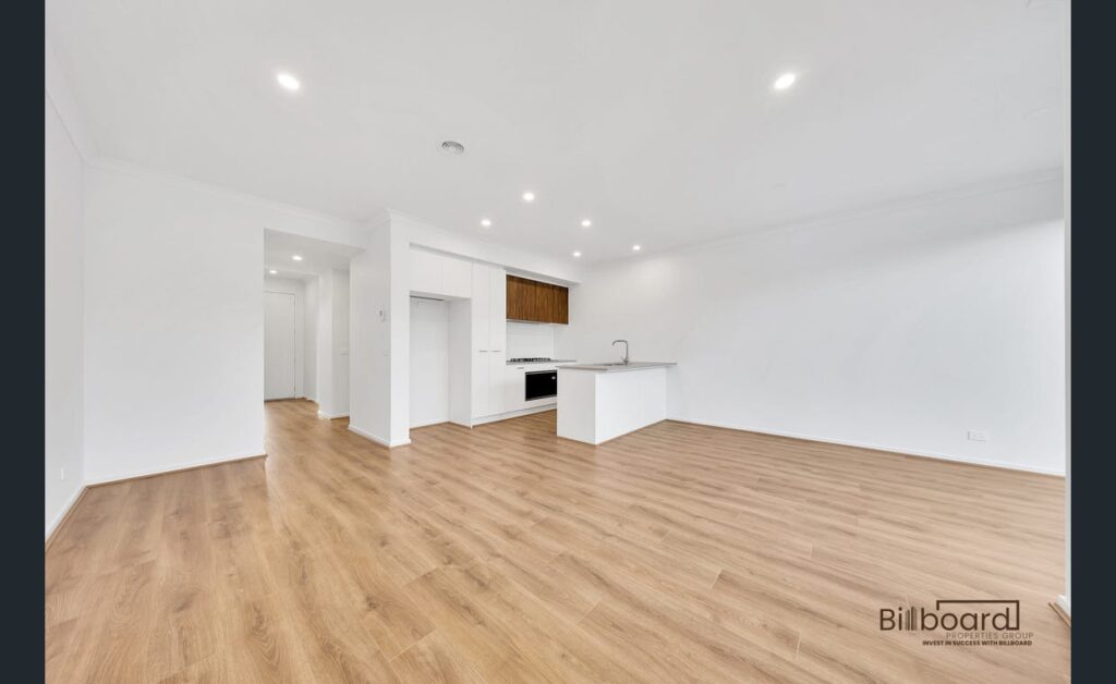 Spacious open plan living and kitchen area with timber flooring, white walls and modern minimalist interior design in a Melbourne home.