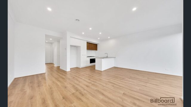 Spacious open plan living and kitchen area with timber flooring, white walls and modern minimalist interior design in a Melbourne home.