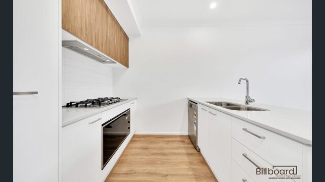 Modern white kitchen with wooden overhead cabinetry, gas cooktop, built-in oven, dishwasher and timber flooring in a contemporary Melbourne home.