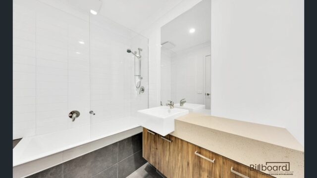 Bright white bathroom with bathtub, wooden vanity unit and modern shower fittings in a contemporary Melbourne home.