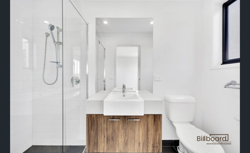 Modern bathroom with glass shower, wooden vanity cabinet and white basin in a contemporary Melbourne property.