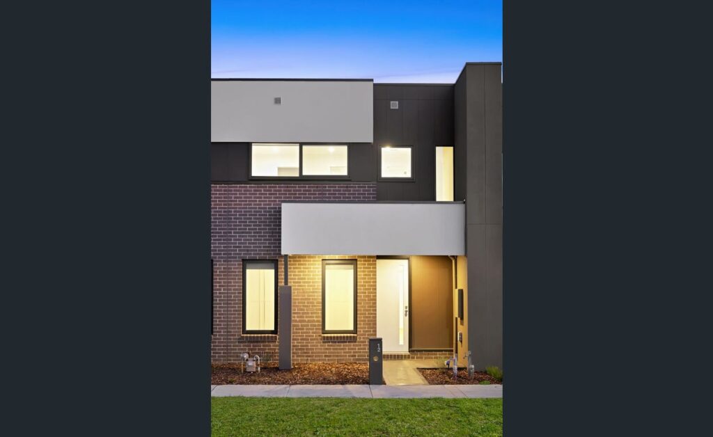 Modern double-storey townhouse exterior with brick and render finish, illuminated entry and contemporary architectural design in Wollert.