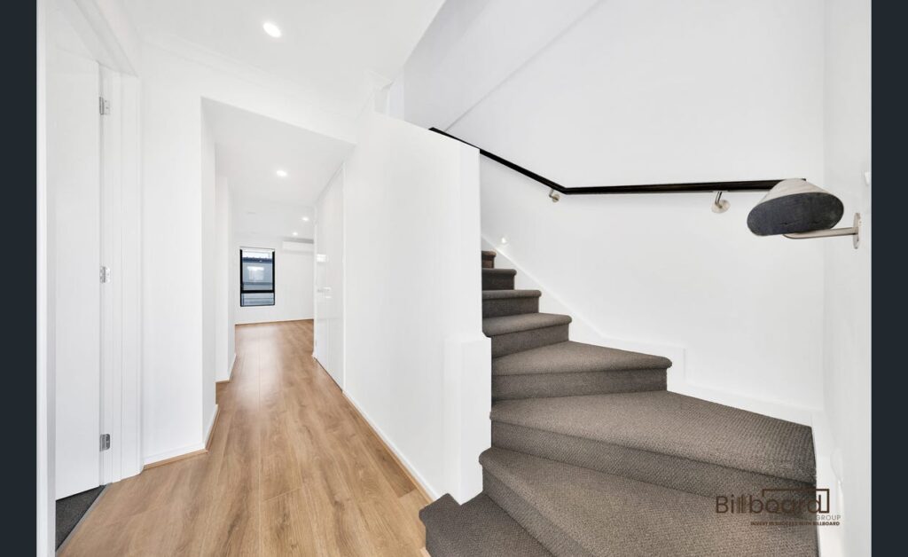 Bright internal hallway with timber flooring and carpeted staircase in a modern Melbourne home.