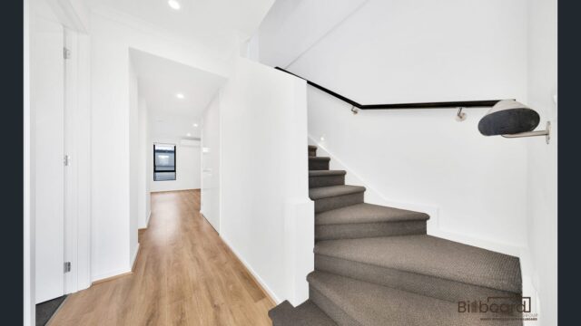Bright internal hallway with timber flooring and carpeted staircase in a modern Melbourne home.