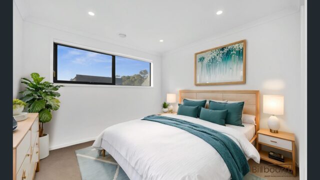 Beautifully furnished bedroom with wooden bed frame, teal accent decor, bedside lamps and large window providing natural light in a modern Melbourne home.