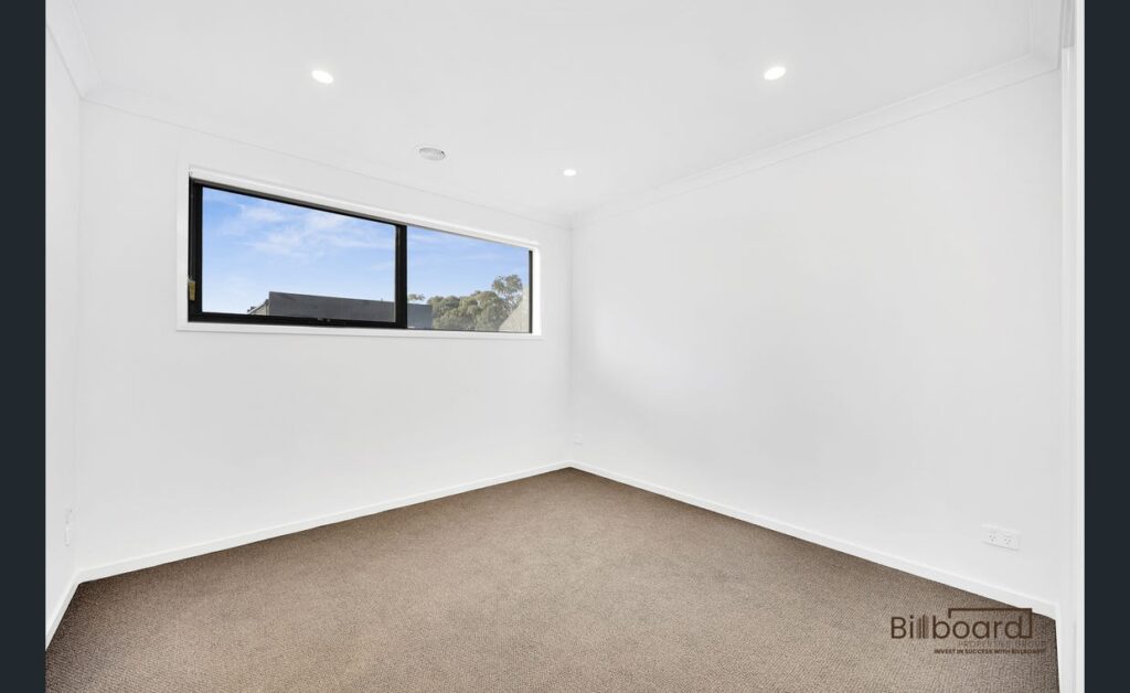 Empty bedroom with carpet flooring, white walls and a wide horizontal window in a modern Melbourne home.
