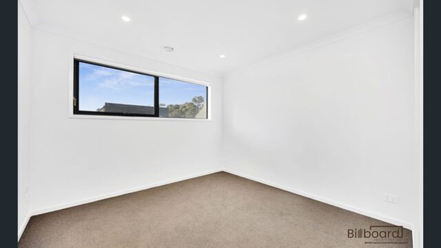 Empty bedroom with carpet flooring, white walls and a wide horizontal window in a modern Melbourne home.