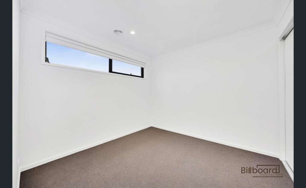Empty bedroom with white walls, carpet flooring and high horizontal window in a modern Melbourne home.
