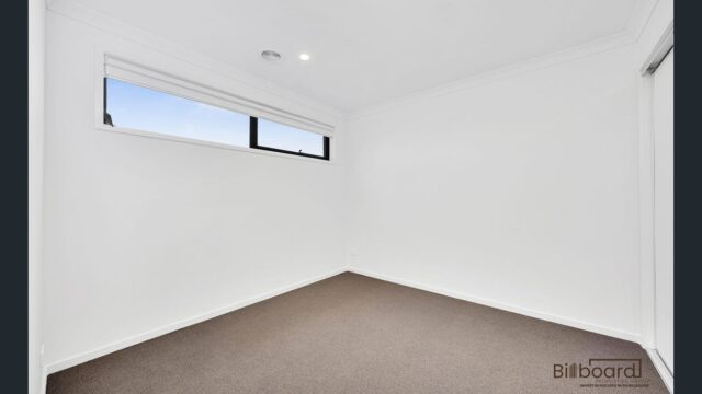 Empty bedroom with white walls, carpet flooring and high horizontal window in a modern Melbourne home.