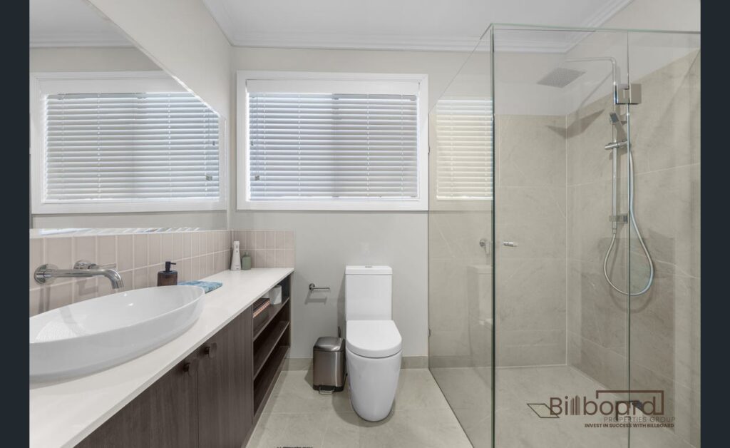Modern bathroom with a glass walk-in shower, white toilet, floating vanity with vessel sink, large mirror, tiled walls and flooring, and two windows with blinds allowing natural light in.