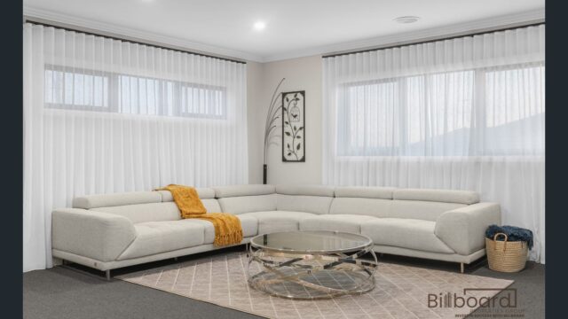 Stylish lounge area with a large cream L-shaped sofa, golden throw blanket, modern glass round coffee table, neutral decor accents, and sheer white curtains covering wide windows for a bright and contemporary look.