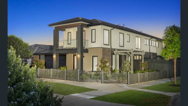 Modern two-storey home on a corner block featuring a stylish architectural design with balcony, mixed exterior materials, landscaped front garden and fenced yard, captured during evening with a clear blue sky.