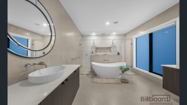 Spacious modern bathroom with a freestanding bathtub, large glass-enclosed walk-in shower, floating vanity with round mirror, and floor-to-ceiling beige tiles, featuring frosted windows for privacy and a clean luxury design.