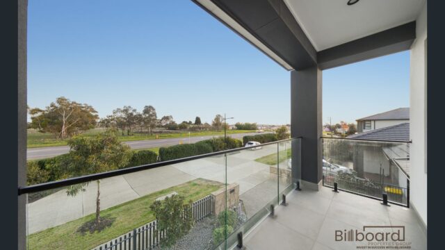 Modern balcony with tiled flooring and clear glass balustrade overlooking the street and nearby greenery, providing an open outdoor sitting area with views towards the surrounding neighbourhood.