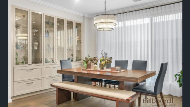 Elegant dining room with a wooden dining table, bench seating, cushioned dining chairs, ceiling chandelier light, large glass display cabinetry, and sheer curtains providing soft natural light into the space.