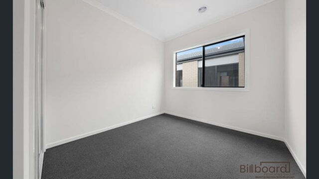 Simple empty bedroom with grey carpet, white walls and large window in a contemporary Melbourne home.