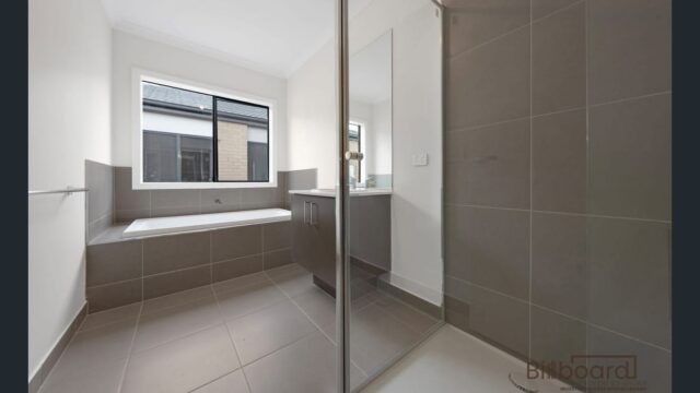 Modern bathroom with built-in bathtub, glass shower, grey tiled flooring and large window providing natural light in a Melbourne home.