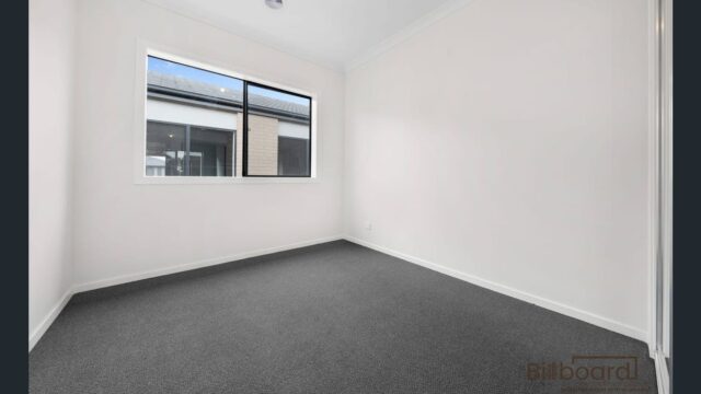 Unfurnished bedroom with grey carpet, white walls and large window providing natural light in a modern Melbourne home.