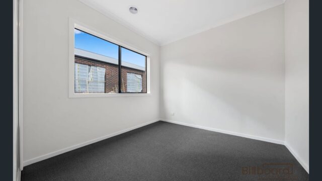 Empty bedroom with grey carpet flooring, large window and neutral white walls in a modern Melbourne home.