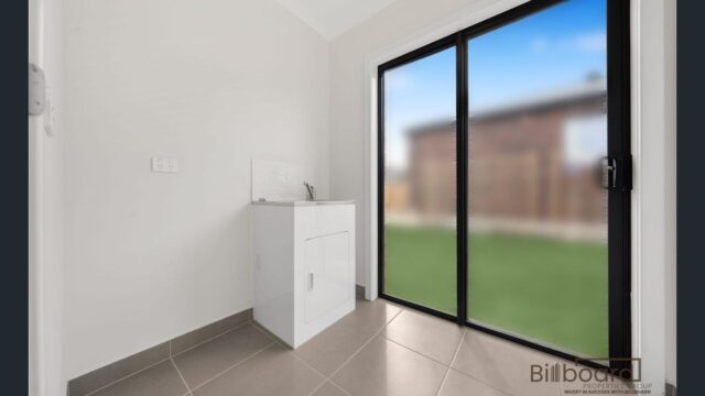 Modern laundry space with tiled flooring, laundry sink and sliding glass doors opening to the backyard in a Melbourne home.