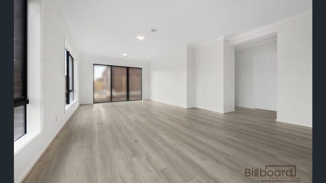 Spacious empty living room with wide timber flooring, large windows and sliding glass doors in a contemporary Melbourne home.