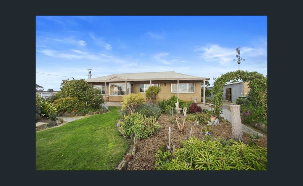 Farmhouse with well-maintained garden, green lawn and landscaped plants set in open rural countryside.