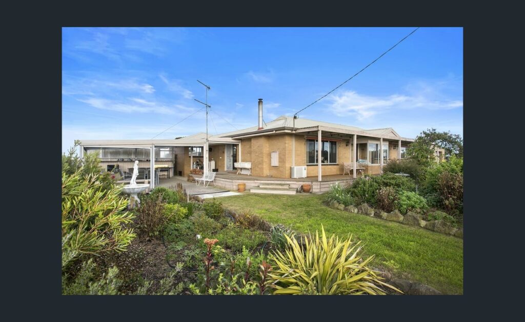 Single-storey farmhouse with outdoor seating area, landscaped garden and open countryside surroundings under a blue sky.