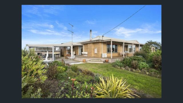 Single-storey farmhouse with outdoor seating area, landscaped garden and open countryside surroundings under a blue sky.