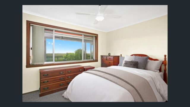 Cozy farmhouse style bedroom with wooden furniture, ceiling fan and large window overlooking green countryside views.
