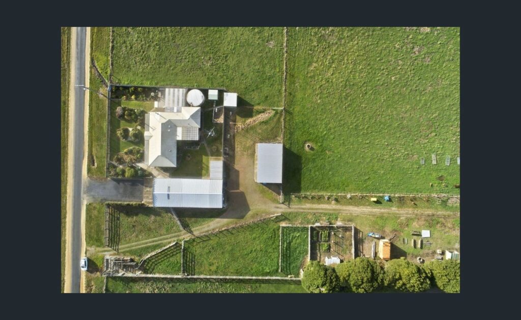 Aerial top view of rural farm property showing house, sheds, fenced paddocks and surrounding green farmland.