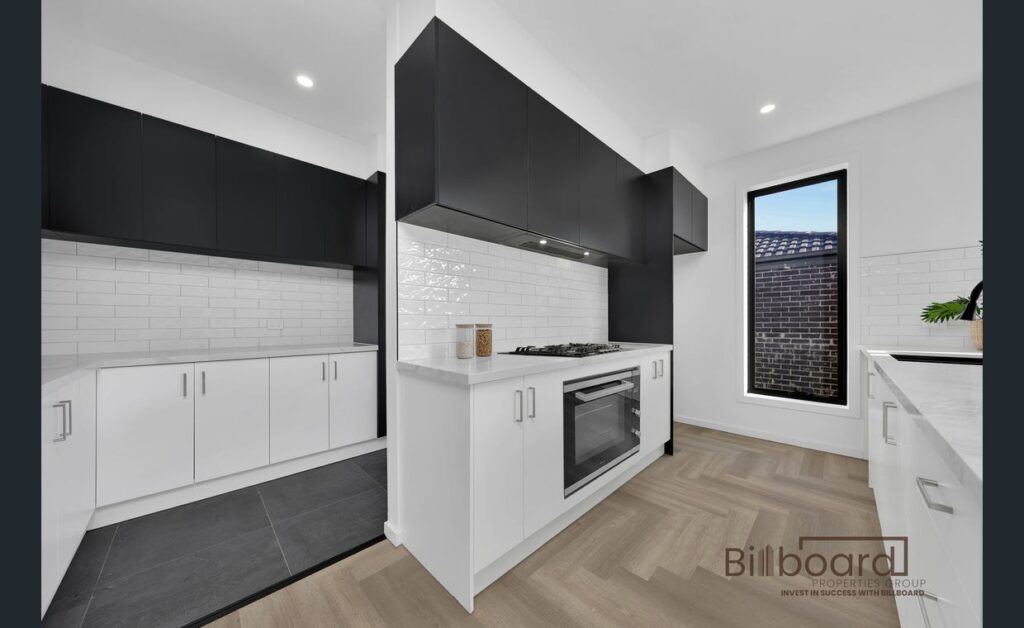 Contemporary kitchen with white cabinetry, black overhead cupboards, gas cooktop, and herringbone flooring in a modern Melbourne home.
