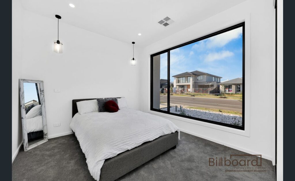 Modern bedroom with large floor-to-ceiling window, contemporary pendant lights and minimal interior styling overlooking the street in a Melbourne home.