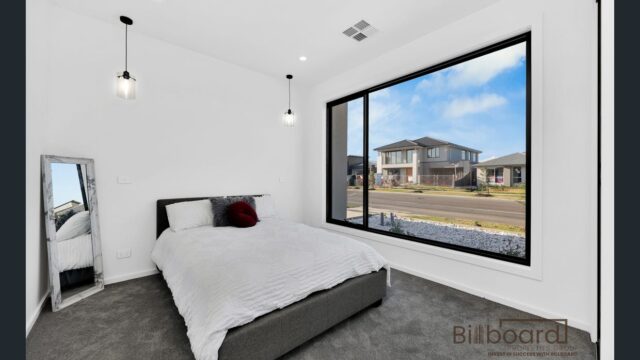 Modern bedroom with large floor-to-ceiling window, contemporary pendant lights and minimal interior styling overlooking the street in a Melbourne home.