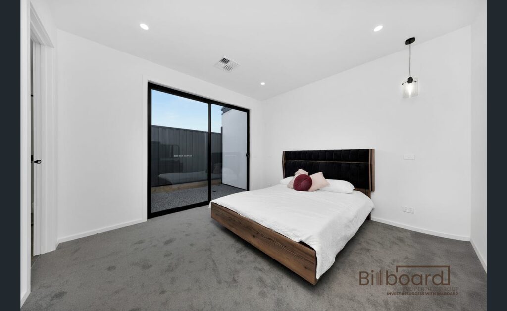 Spacious modern bedroom with minimalist bed frame, sliding glass door to outdoor area, and clean white interior design in a Melbourne home.