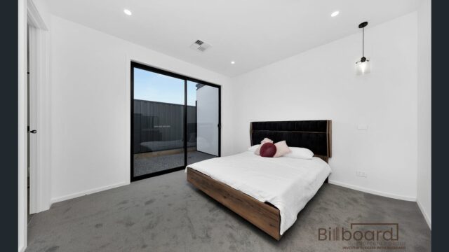 Spacious modern bedroom with minimalist bed frame, sliding glass door to outdoor area, and clean white interior design in a Melbourne home.