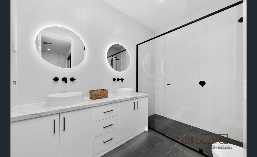 Luxury modern bathroom with double vanity, circular LED mirrors, white cabinetry and large glass shower in a contemporary Melbourne home.