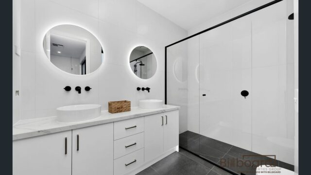 Luxury modern bathroom with double vanity, circular LED mirrors, white cabinetry and large glass shower in a contemporary Melbourne home.